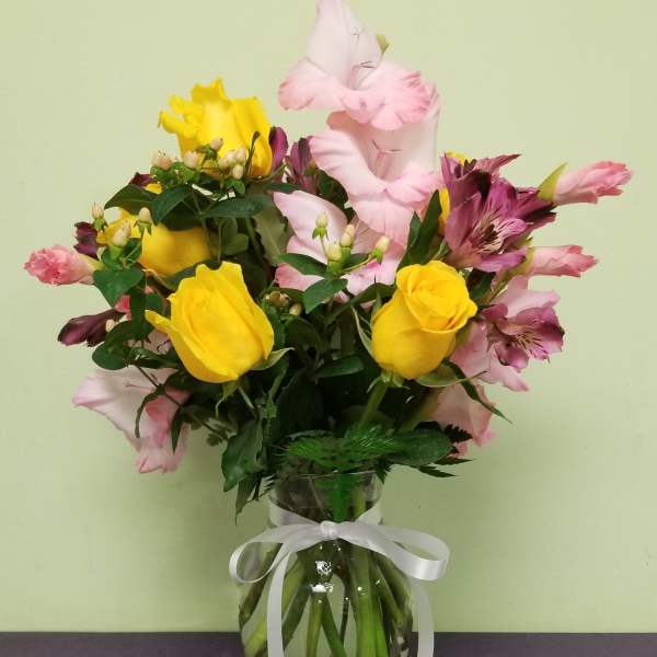 Bouquet of yellow roses and pink alstroemeria in a glass vase with a white ribbon