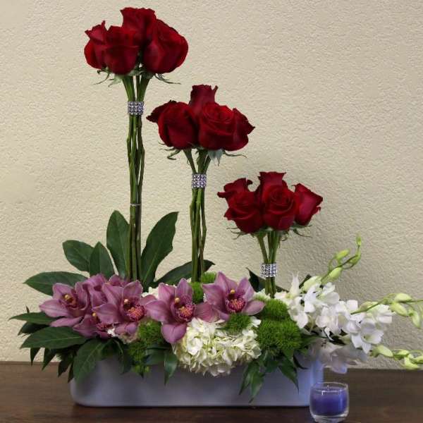 Red roses and purple orchids arranged in a low rectangular container