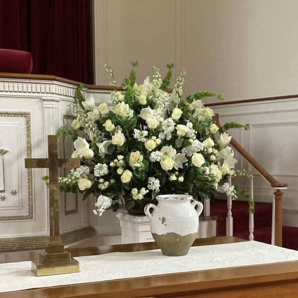 Large white floral arrangement beside a wooden cross in a church