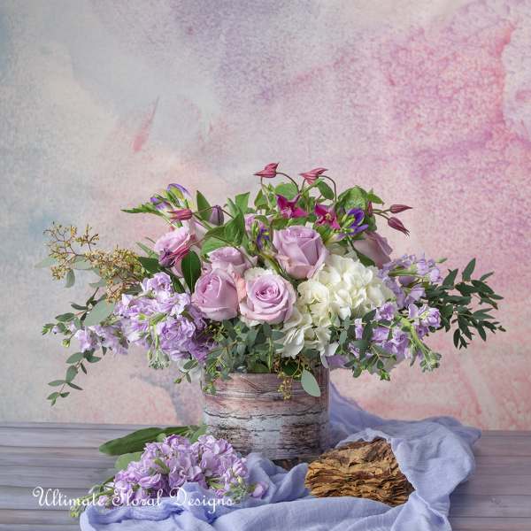 Lavender and white floral arrangement in a rustic container with loose greenery