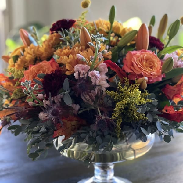 Autumn bouquet in a clear glass pedestal vase with orange and burgundy blooms