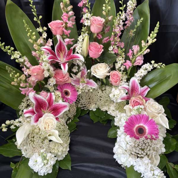 Pink and white floral funeral spray with lilies, roses, and gerbera daisies