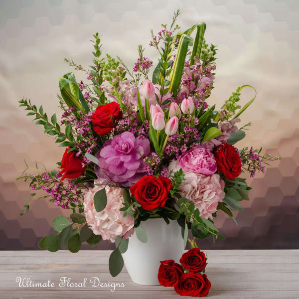 Mixed bouquet of red roses, pink tulips, and hydrangeas in a white vase