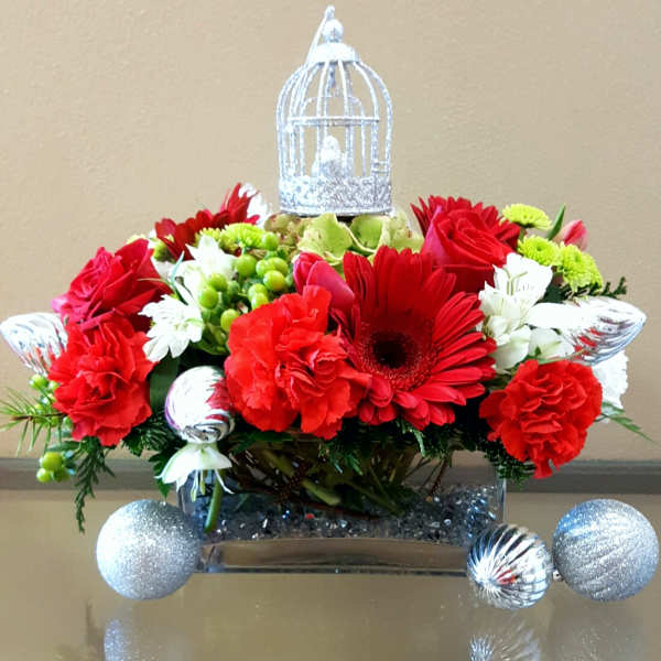 Red flowers arranged with silver ornaments and a decorative birdcage topper