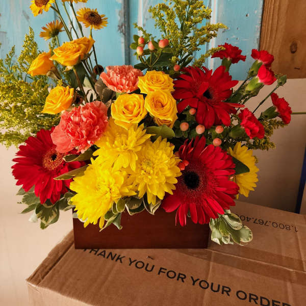 Bright mixed bouquet with red gerberas, yellow roses, and carnations in a box