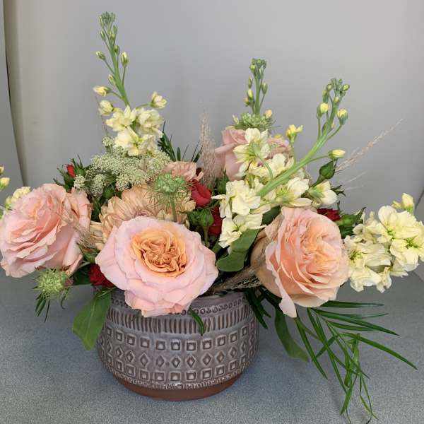 Low floral arrangement of pink roses and cream blooms in a patterned ceramic vase