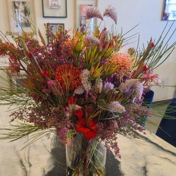 Large mixed bouquet in a clear glass vase with spiky blooms and red accents