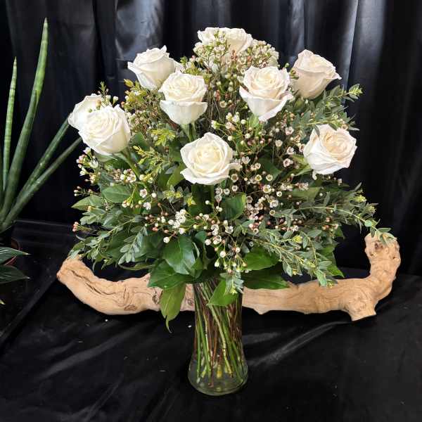 White roses arranged in a glass vase with greenery and small filler flowers