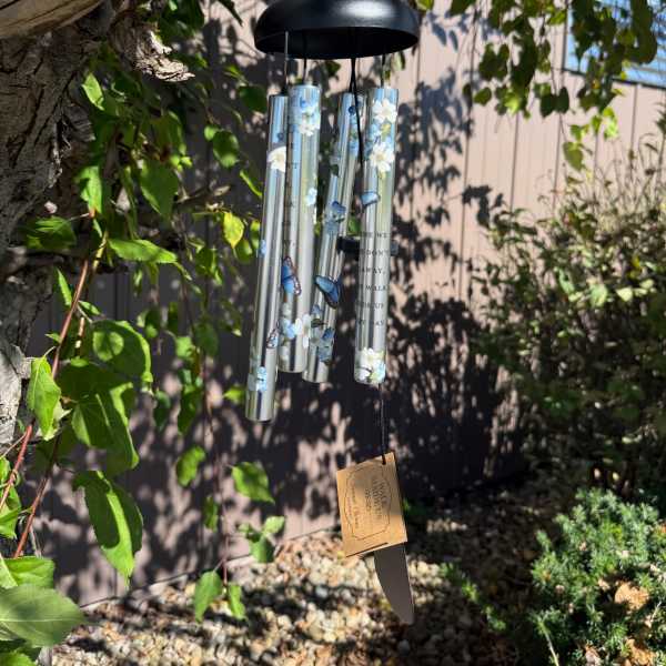 Decorative silver wind chime with blue butterflies and white flowers hanging from a tree branch