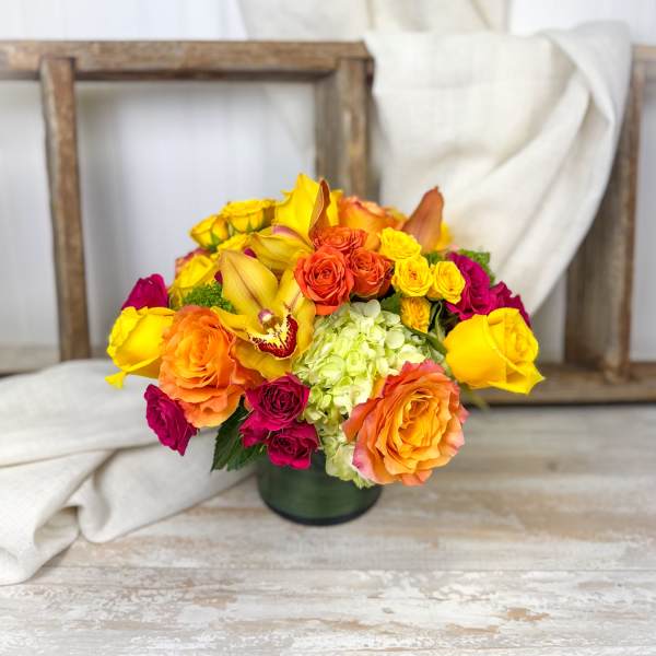 Bouquet of yellow, orange, and pink roses in a dark vase
