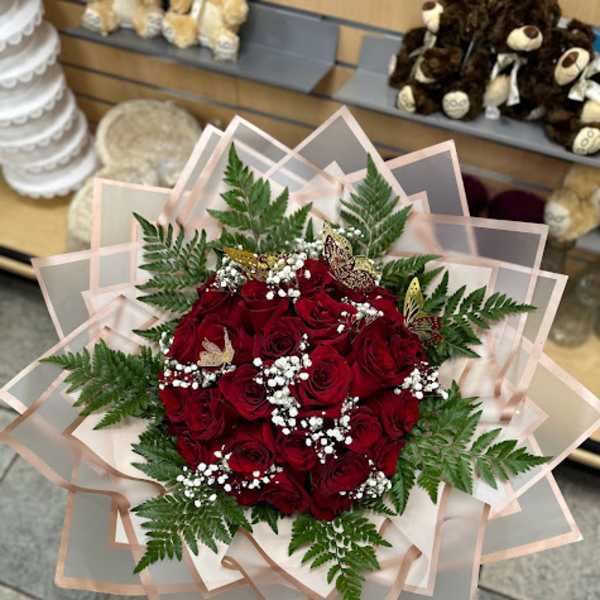 Bouquet of red roses with baby's breath and fern foliage in layered pink wrap