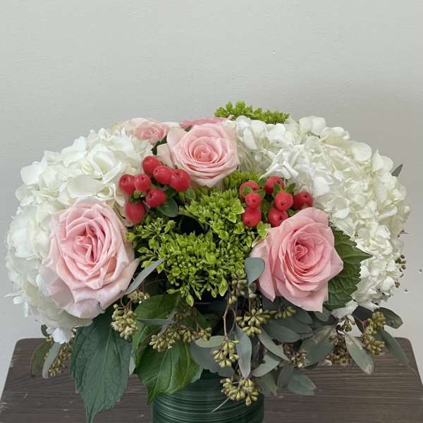 Pink roses and white hydrangeas in a glass vase with red berries