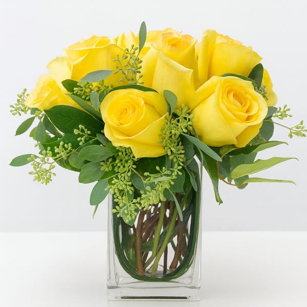 Yellow roses arranged in a clear glass vase with greenery