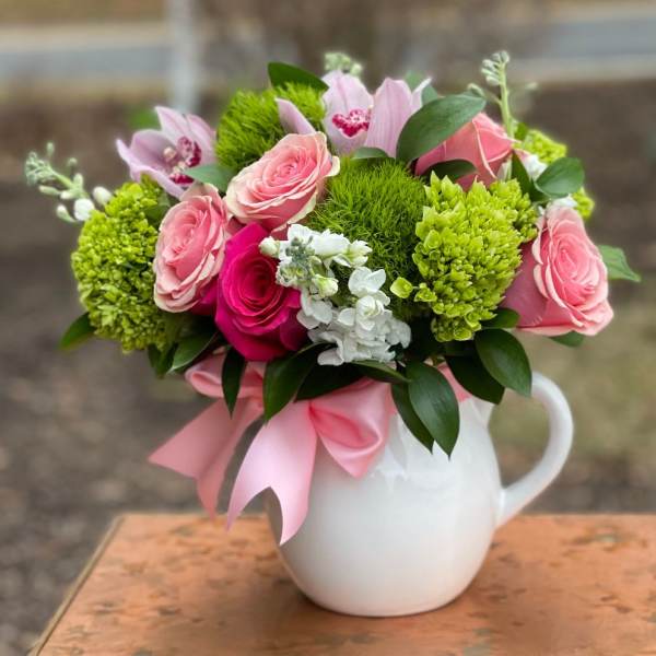Pink roses and green blooms arranged in a white pitcher vase