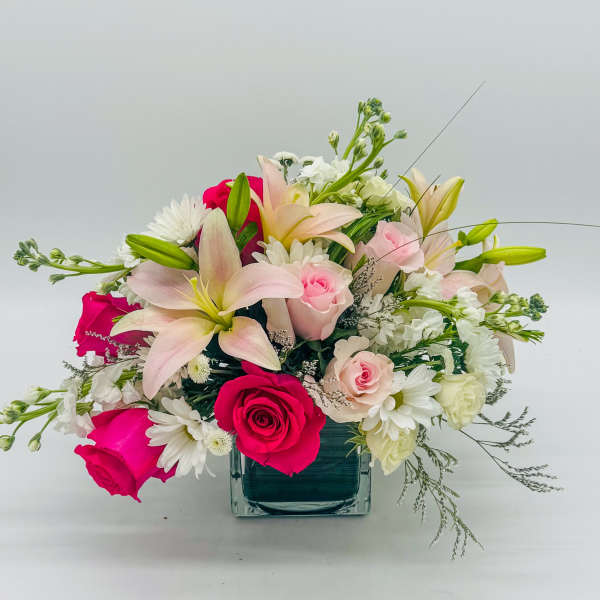 Mixed bouquet of pink roses, lilies, and white daisies in a square glass vase