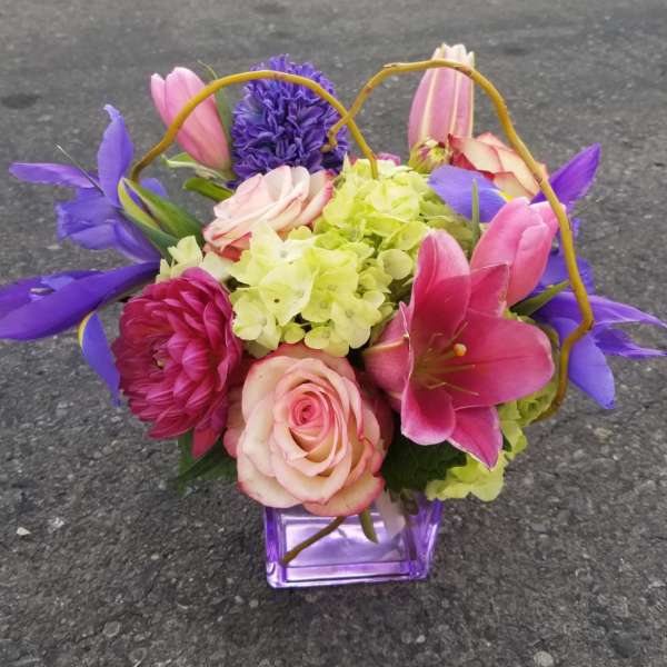 Colorful bouquet in a purple glass vase with roses, lilies, and hydrangea