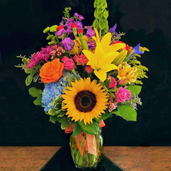 Colorful mixed bouquet with sunflower, lilies, roses, and hydrangea in a glass vase