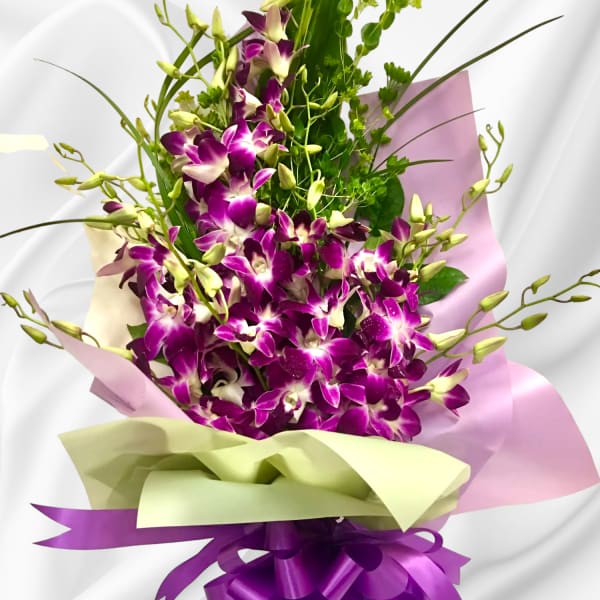 Bouquet of purple orchids wrapped in pink and green paper with a purple ribbon