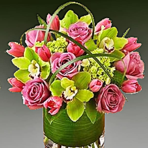 Pink roses and tulips arranged in a glass vase with green orchids