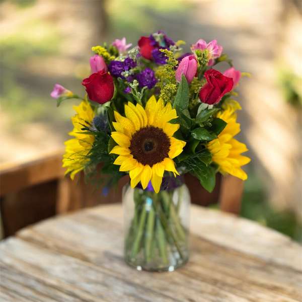 Bouquet of sunflowers, roses, and mixed blooms in a glass vase