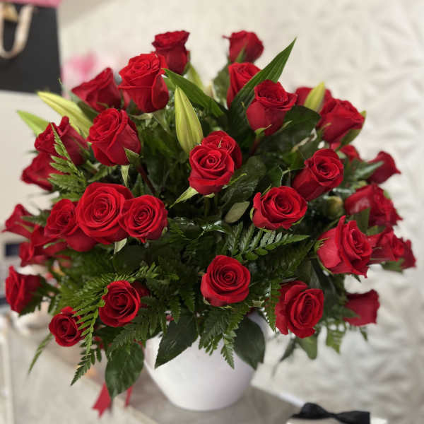 Bouquet of red roses in a white vase with green foliage