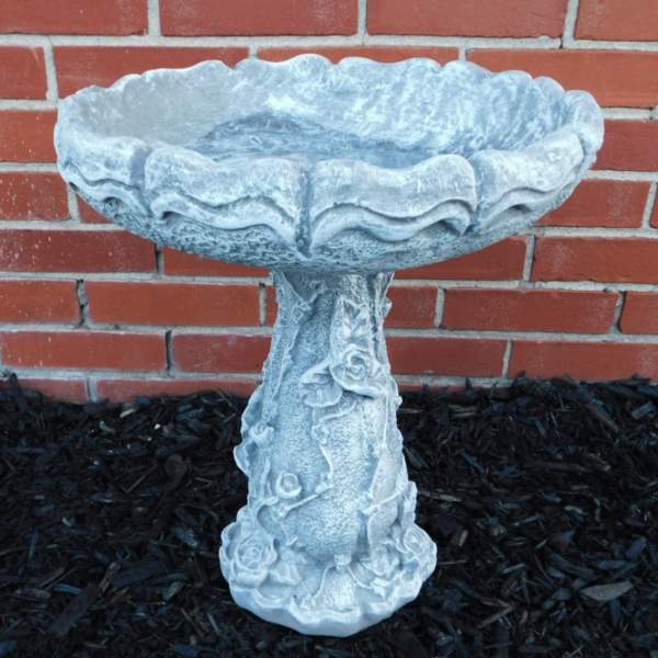Stone birdbath with rose relief against a brick wall