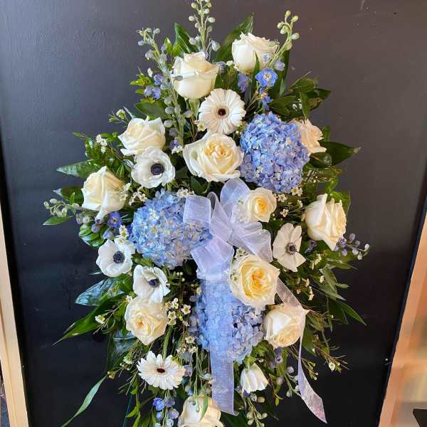 Standing floral spray with white roses, blue hydrangeas, and a ribbon bow
