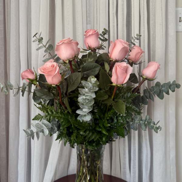 Pink roses arranged in a clear glass vase with eucalyptus foliage