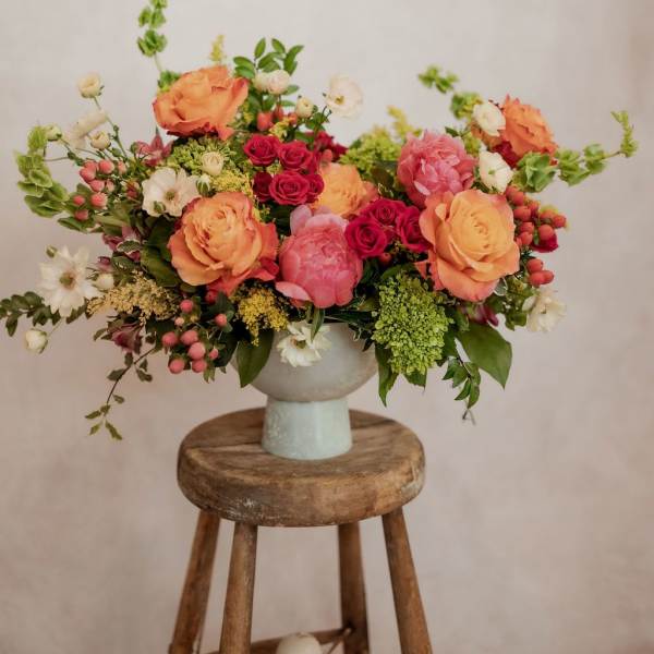Mixed bouquet of peach, pink, and white flowers in a pale vase