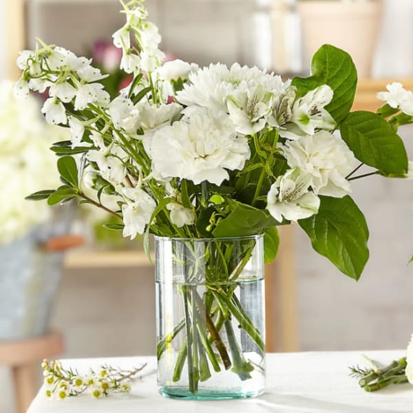 White flowers arranged in a clear glass vase with green leaves
