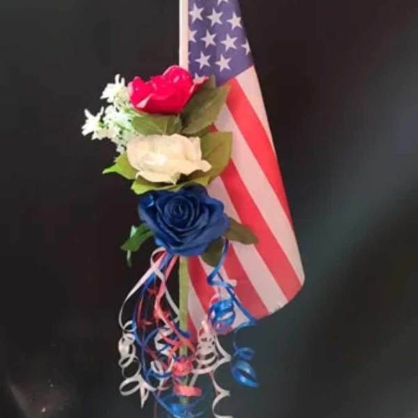 Small floral arrangement with red, white, and blue roses beside an American flag