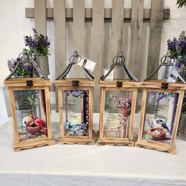 Four wooden lanterns with floral prints and small purple flower arrangements