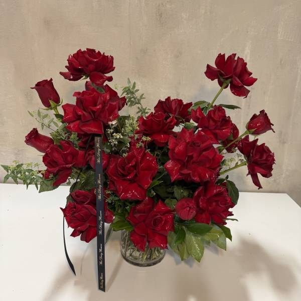Red roses arranged in a clear glass vase with a black ribbon