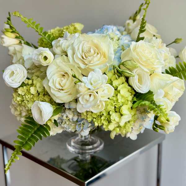White roses and pale blue hydrangeas in a clear glass vase