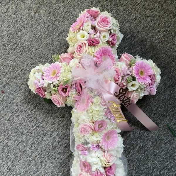 Cross-shaped floral arrangement with pink and white flowers and ribbon