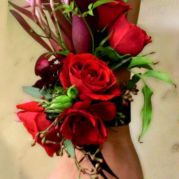 Wrist corsage with red roses and dark purple calla lilies on a black band