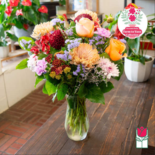 Mixed bouquet of roses, chrysanthemums, and small purple flowers in a glass vase