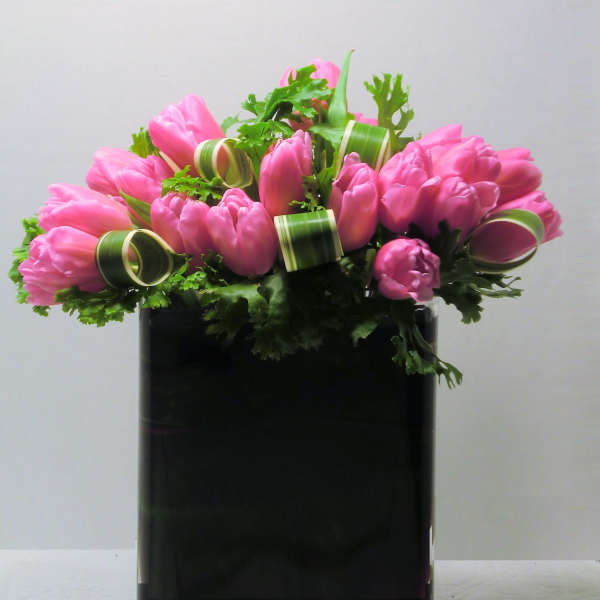 Low arrangement of pink tulips in a rectangular black glass vase with curled accents.