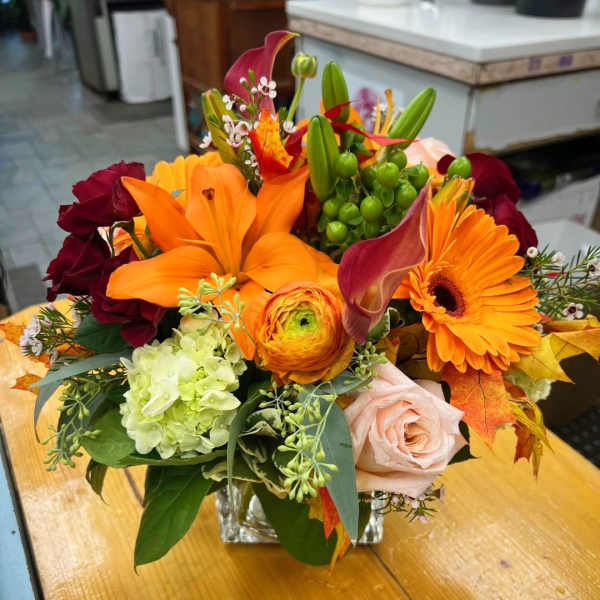 Mixed bouquet with orange lilies, gerbera daisies, and roses in a glass vase