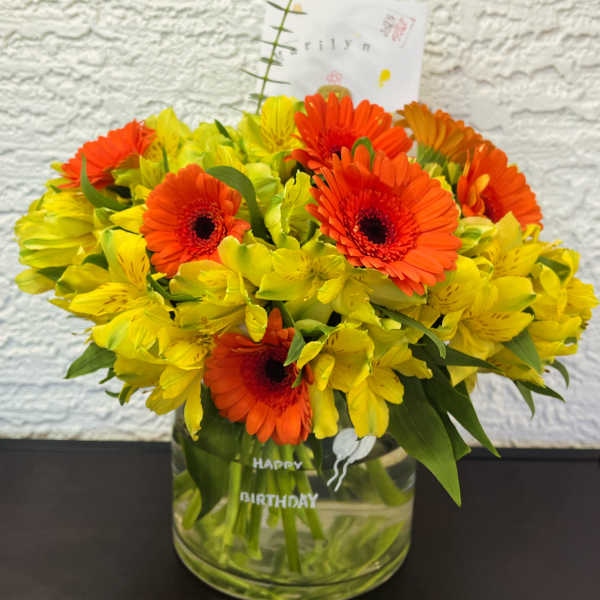 Orange gerbera daisies and yellow alstroemeria in a glass vase