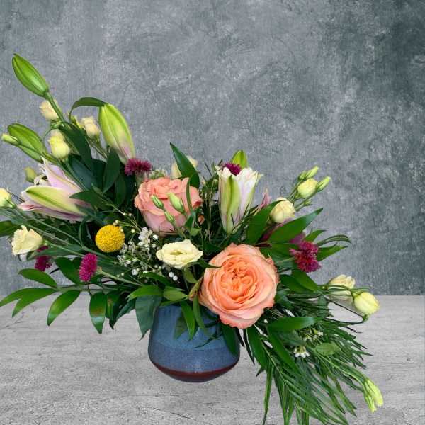 Mixed bouquet with peach roses and lilies in a blue vase