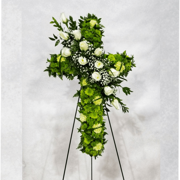 Cross-shaped floral tribute with white roses and green flowers on a stand
