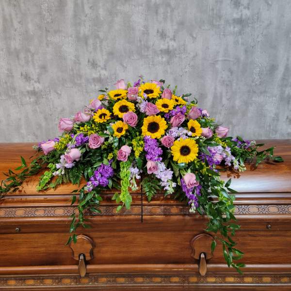 Casket spray with sunflowers, pink roses, and purple flowers