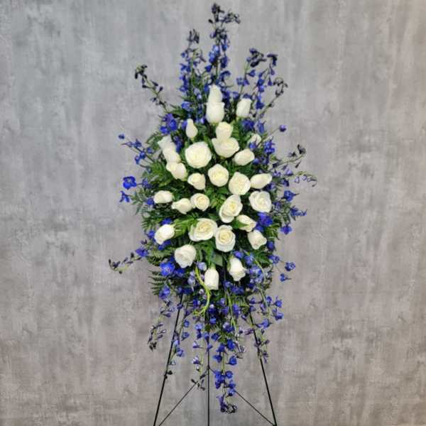 Tall standing spray of white roses and blue flowers on a black easel