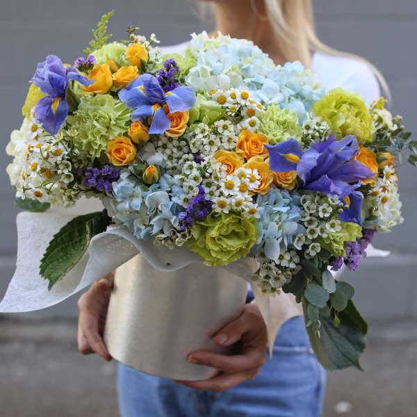 Large bouquet of blue, yellow, and white flowers in a wrapped container