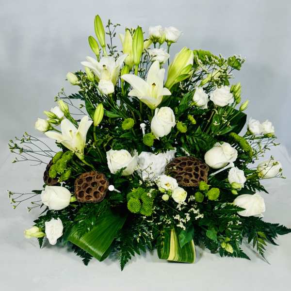White lilies and roses arranged with green accents in a low centerpiece