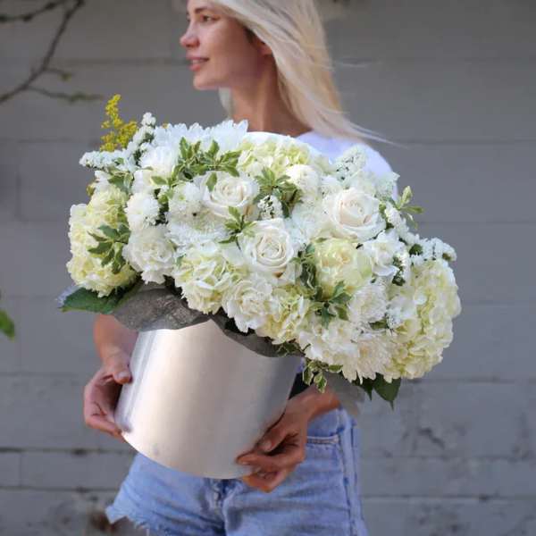 Woman holding a large white floral arrangement in a silver vase