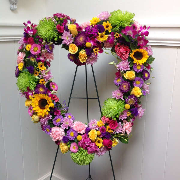 Heart-shaped floral wreath on a black stand with bright mixed flowers