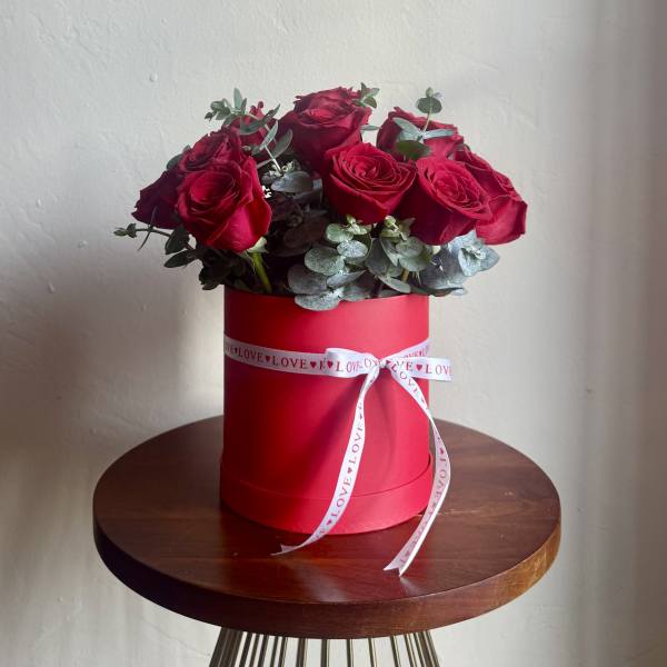 Red roses arranged in a red hat box with a white ribbon