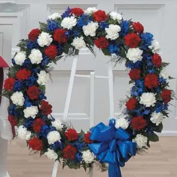 Heart-shaped floral wreath with red, white, and blue flowers on a stand